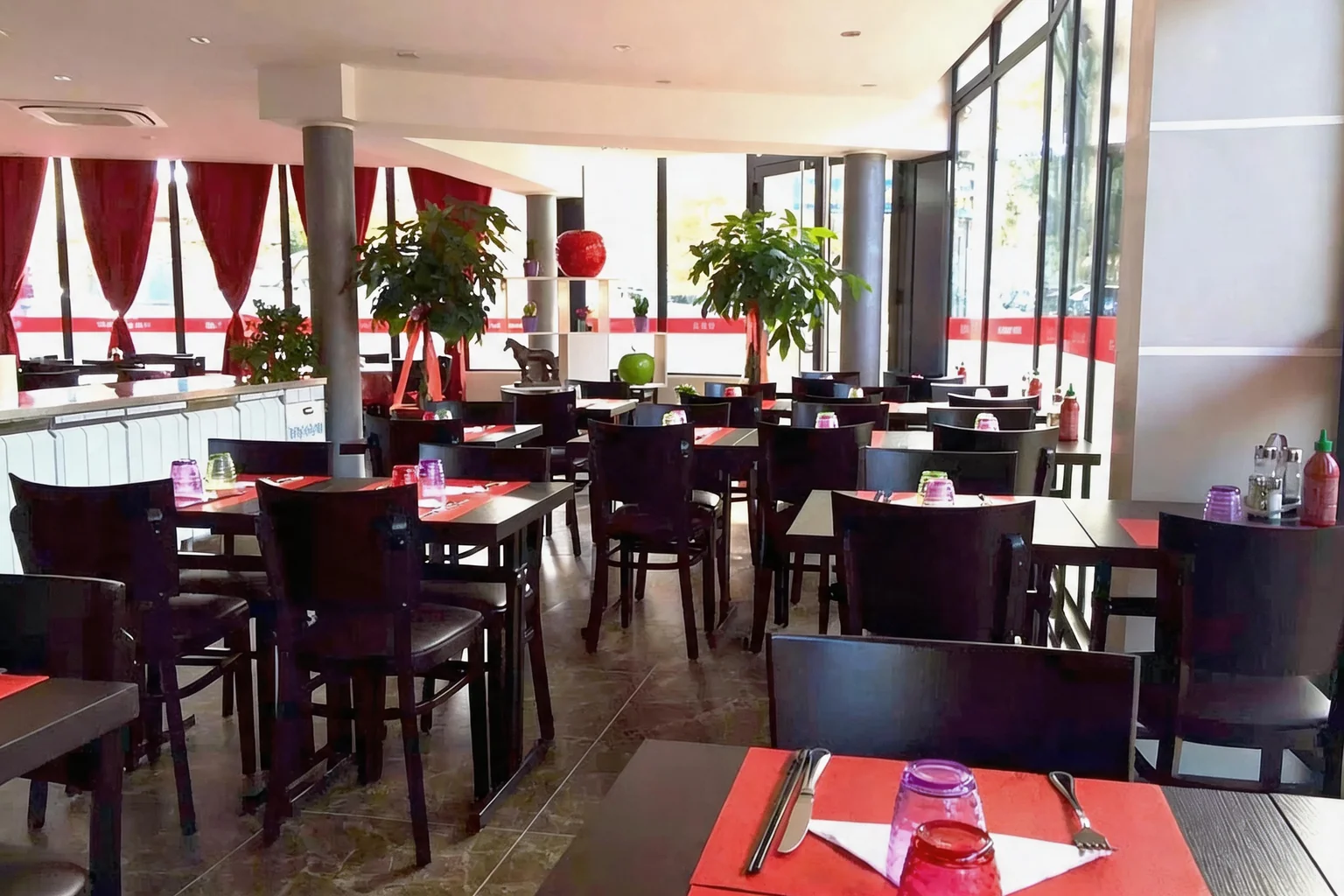 The dining room: dark wooden tables and chairs, red placemats, red curtains